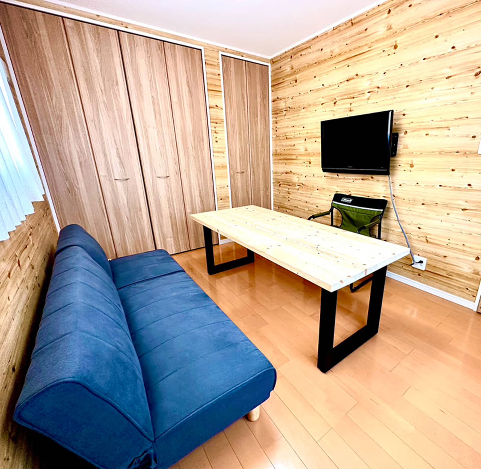 青色のソファーと木製のテーブル、壁には備え付けのテレビが設置されている室内。